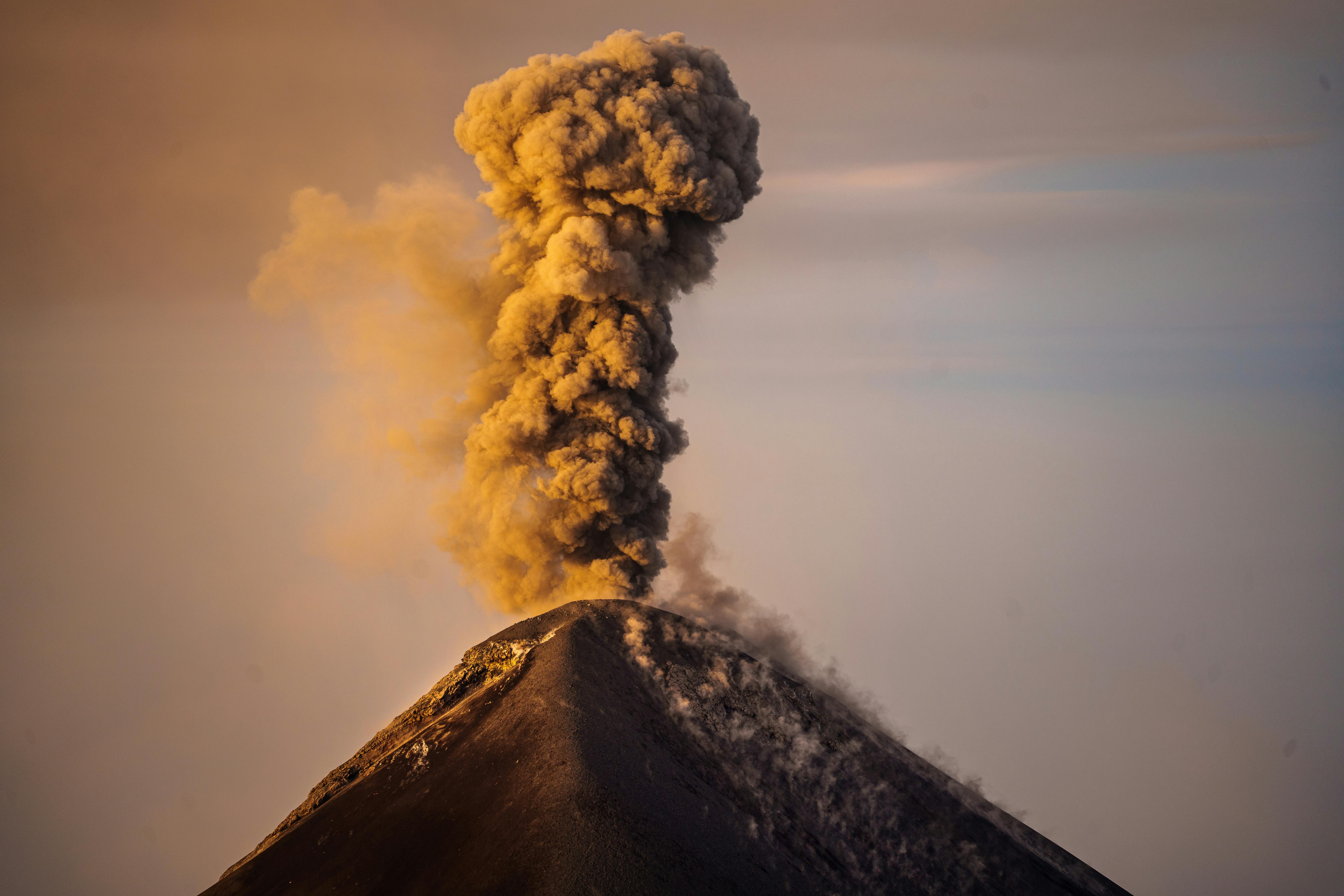 Column of smoke rising from active volcano against sunset background