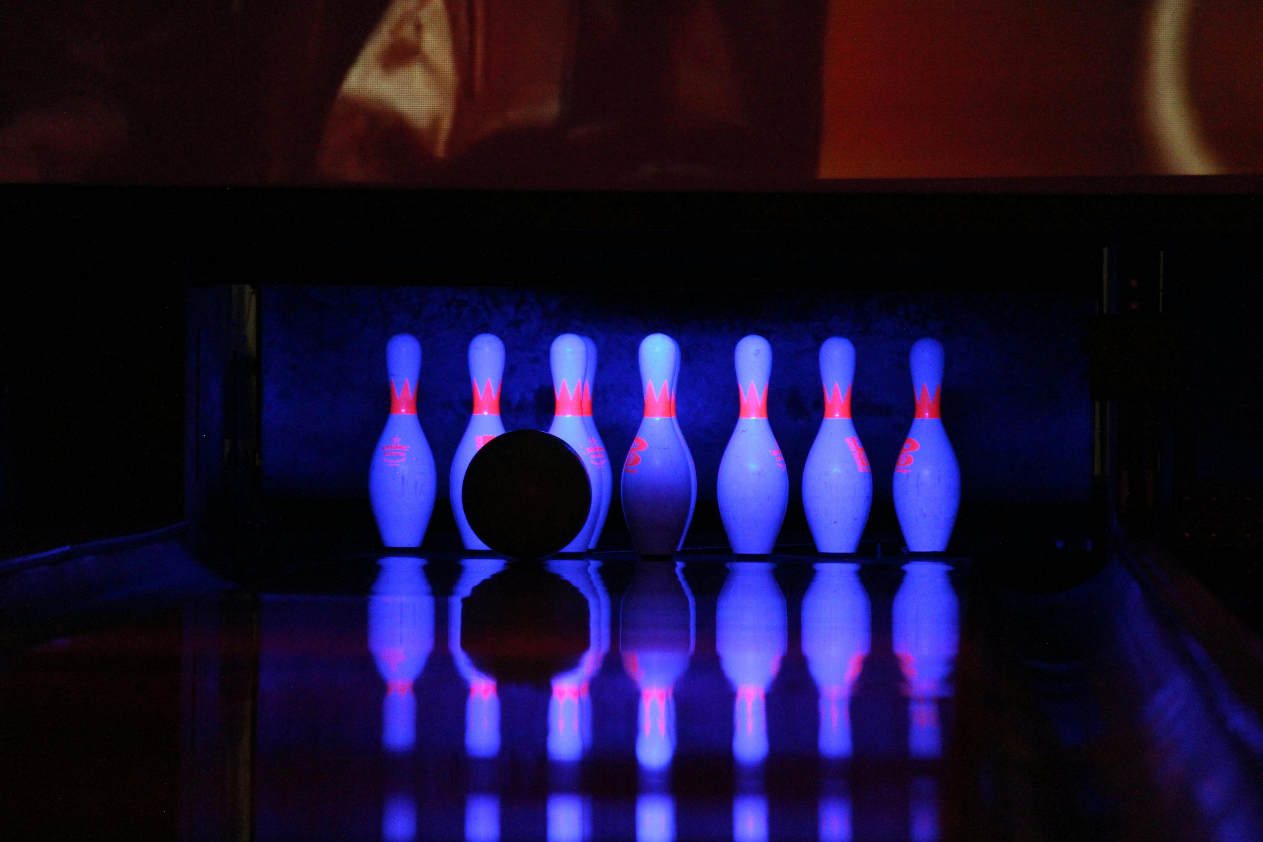 Bowling pings illuminated by neon light with the silhouette of a bowling ball in the foreground