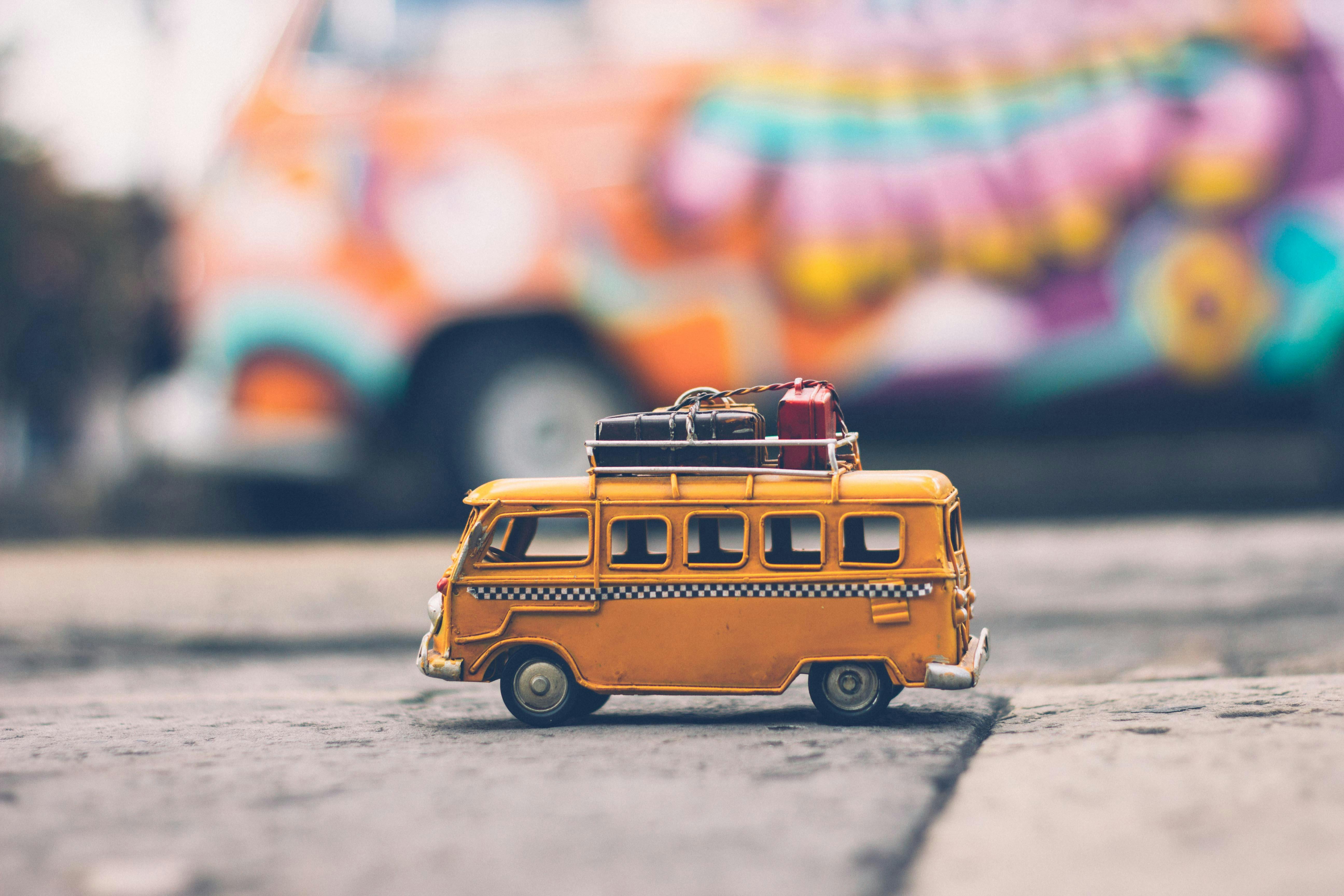 Selective focus photography of yellow taxi bus miniature with blurred similar lifesize bus parked on curb in background